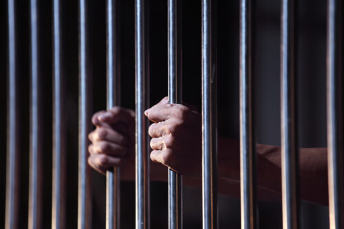 person holding on to jail cell bars