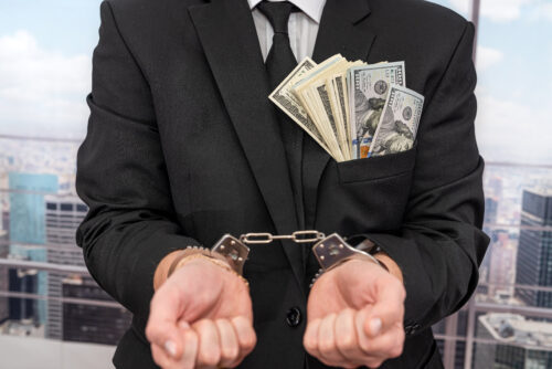 young male businessman in a classic suit and tie holds his hands in handcuffs. The concept of a man in handcuffs